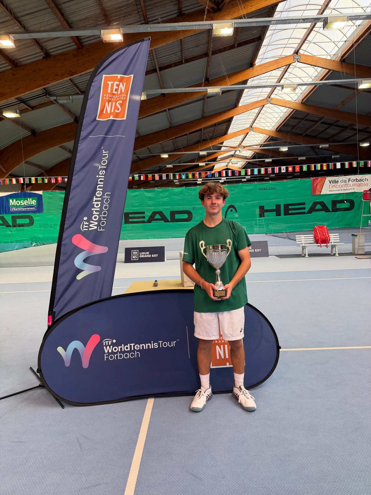 Flynn Thomas hält Trophäe auf ITF World Tennis Tour Forbach Tennisplatz